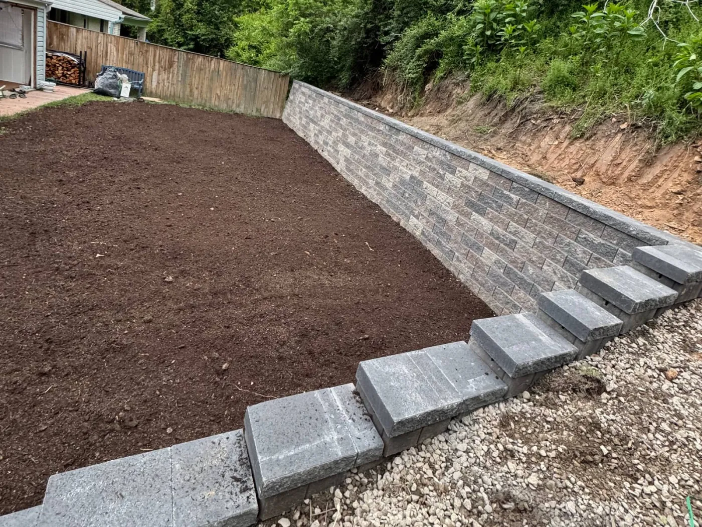 Finished segmental block retaining wall with cap steps holding back a cut slope behind a house