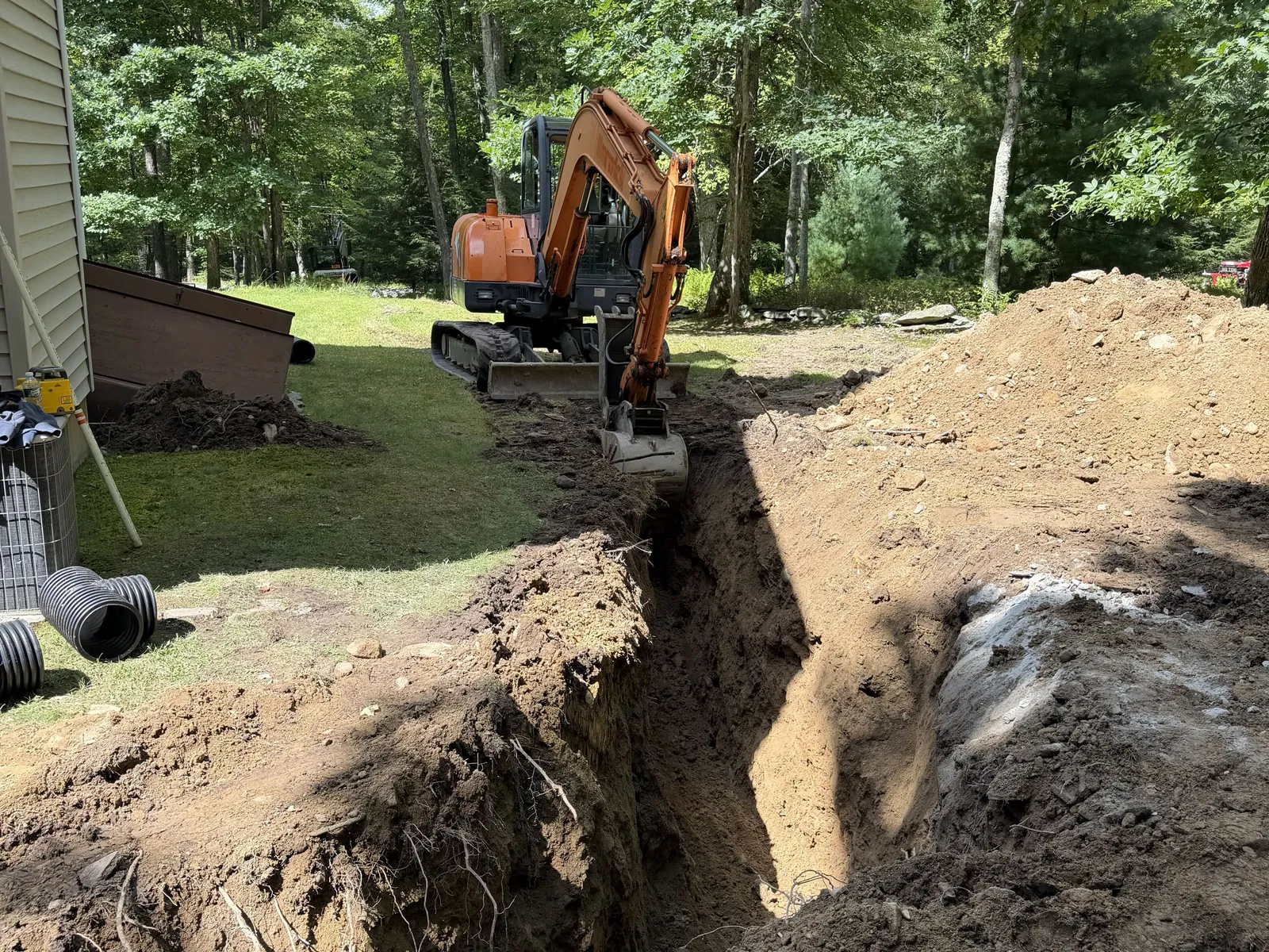 Our mini excavator cutting a drain trench across a wooded residential lot