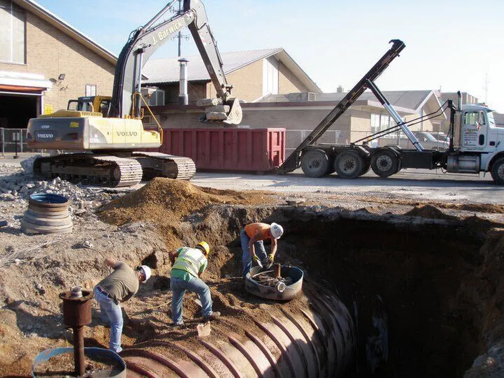 Crew installing large corrugated pipe in an excavation next to an excavator