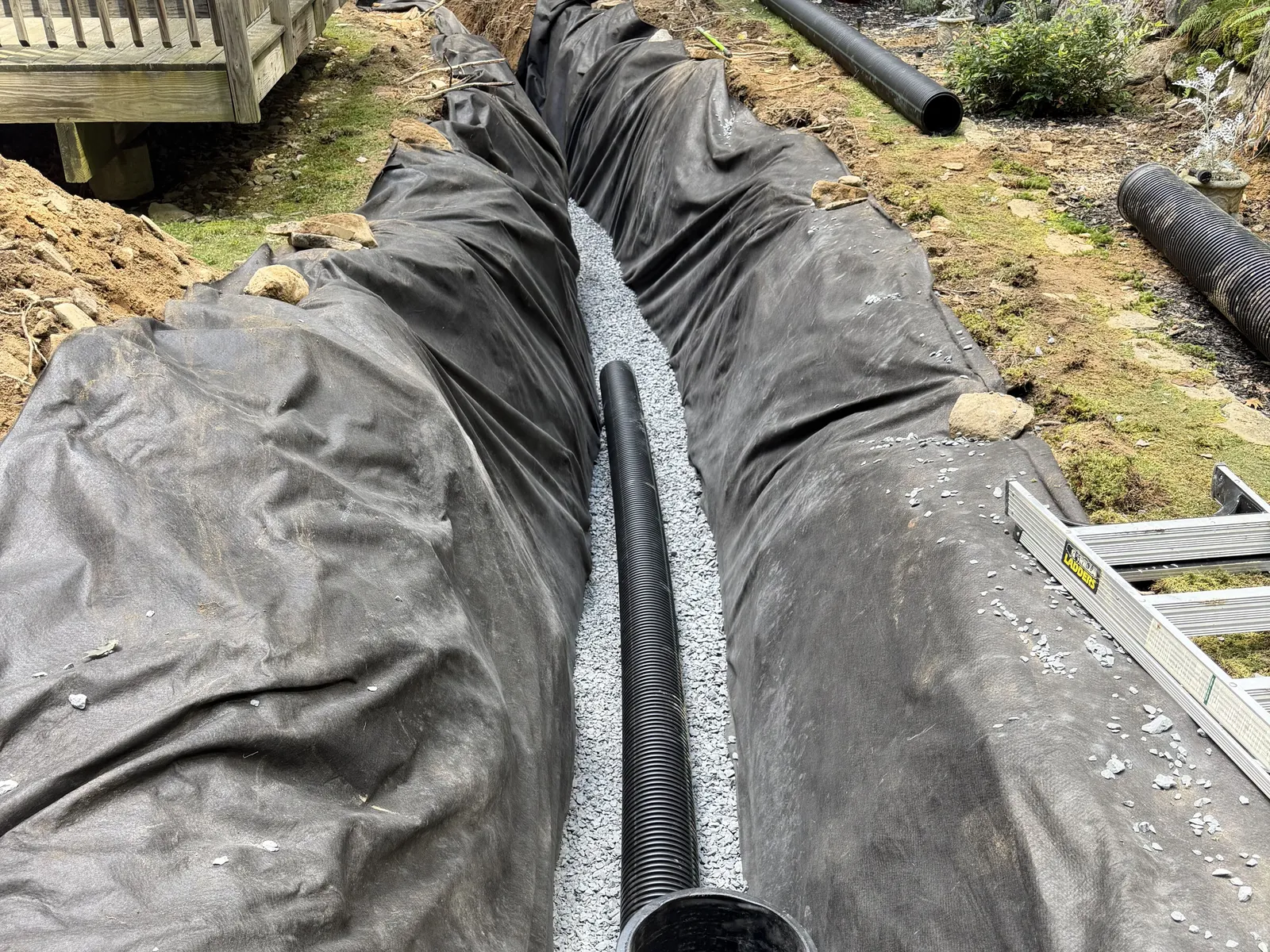 Perforated drain pipe laid on clean stone inside a filter fabric lined trench