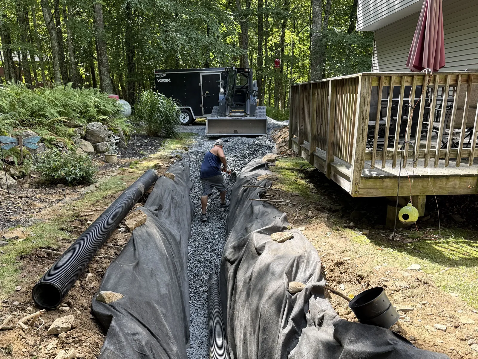 Filter fabric and stone going into a drain trench beside a deck