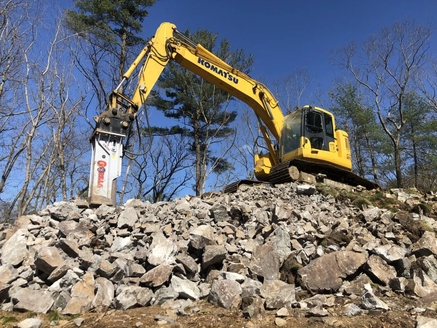 Excavator fitted with a hydraulic breaker standing on a pile of freshly broken rock