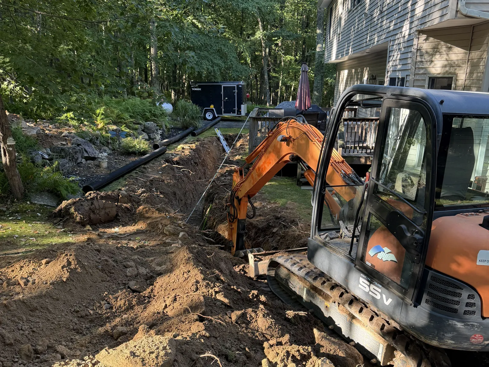 Our mini excavator cutting a trench beside a house on a wooded lot