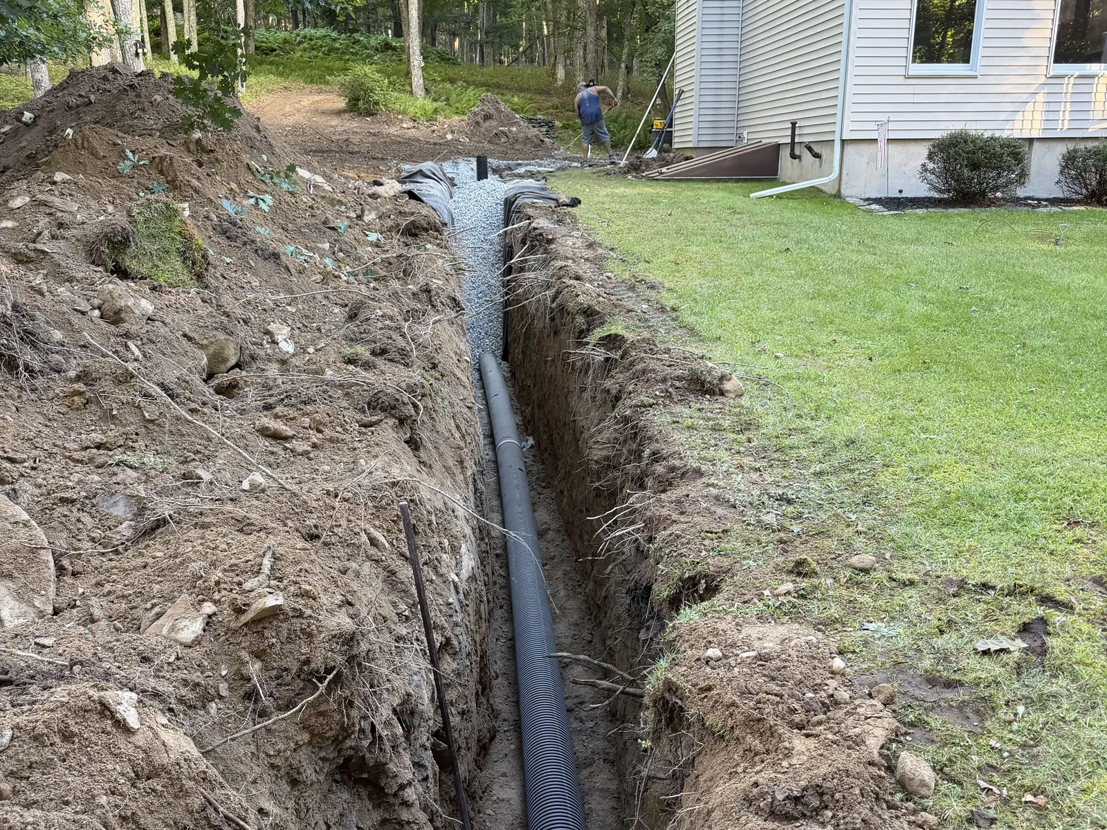 Perforated drain pipe laid in a trench cut along a house and lawn