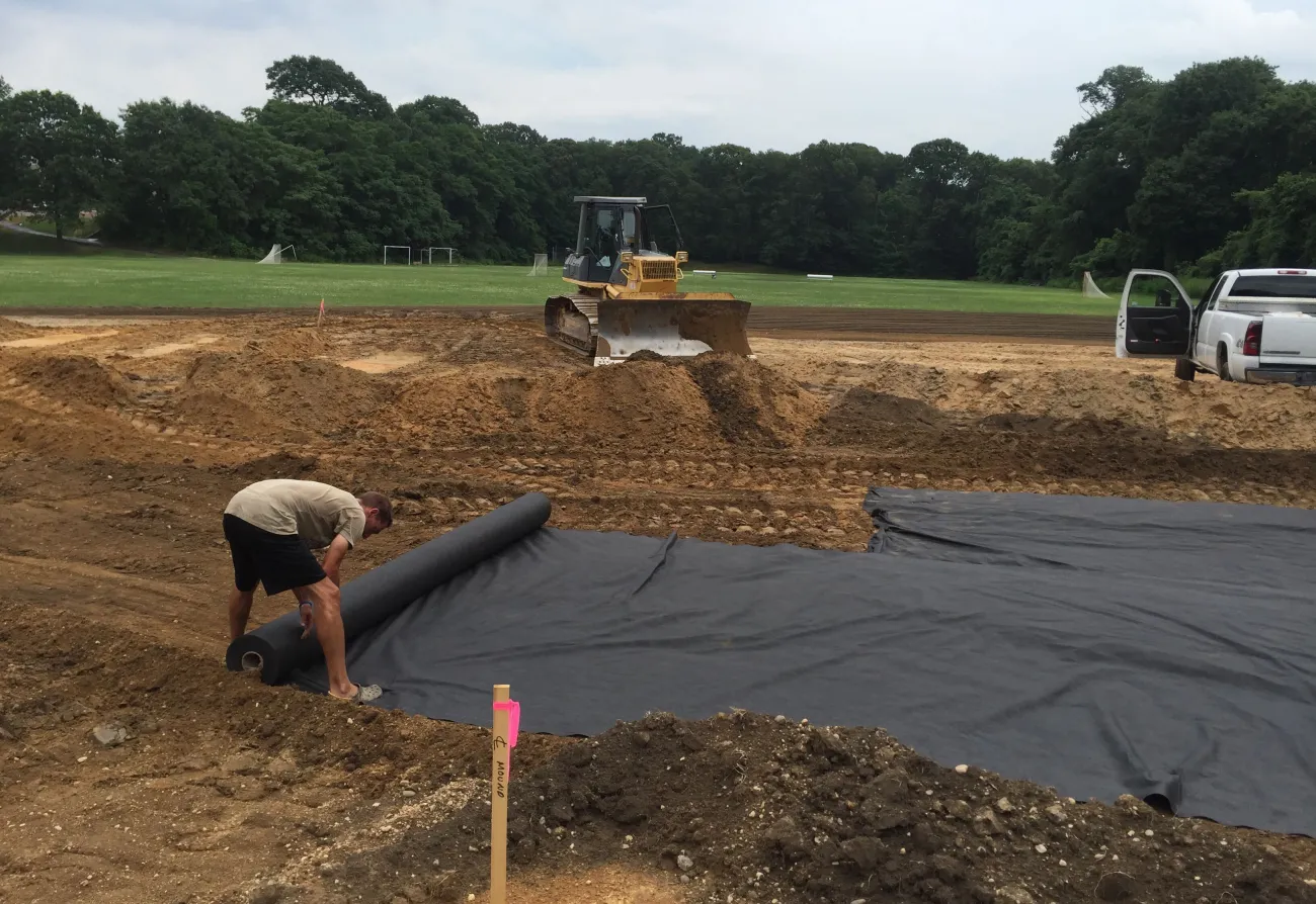 Dozer grading a site while geotextile fabric is rolled out over the subgrade