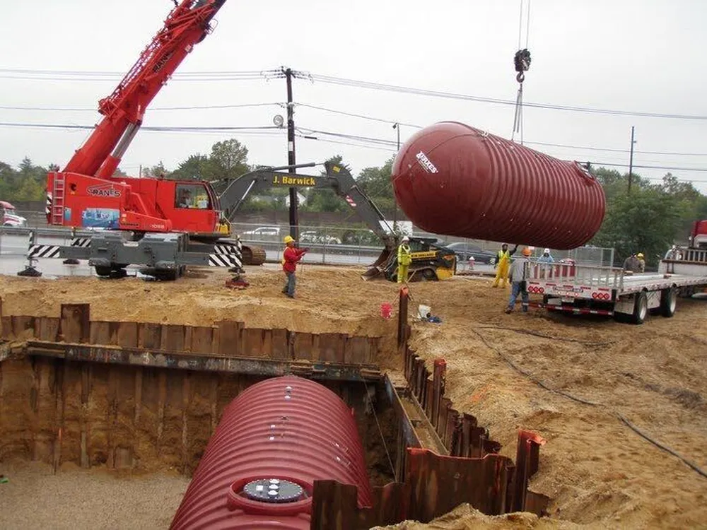 Crane setting a large underground tank into a sheeted excavation